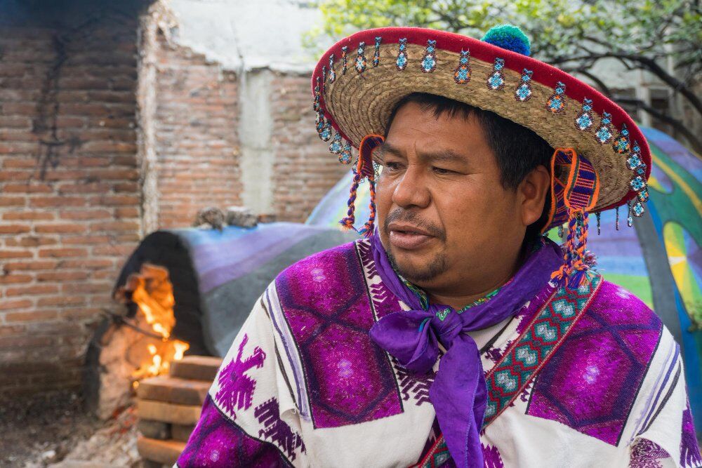 Primer plano de un hombre de la tribu huichol en México y un temazcal al fondo